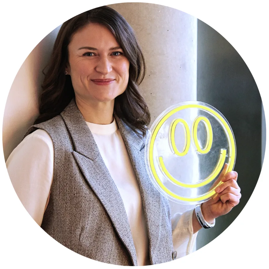 Juliana Bernhardt lächelt und hält ein gelbes Neon-Smiley in die Höhe